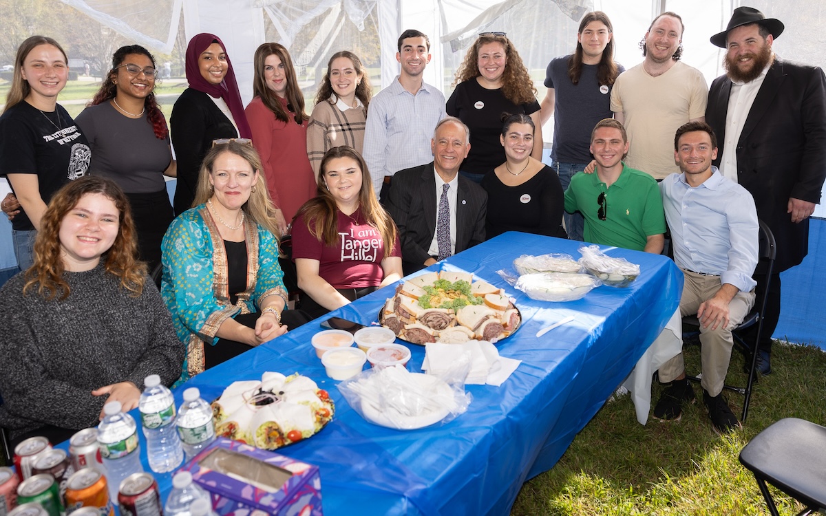 Joshua Koegel (standing, sixth to the left) with his peers, President Michelle J. Anderson, and CUNY Chancellor Félix V. Matos Rodríguez, celebrating the new sukkah on campus.