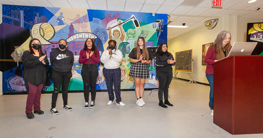 Adjunct Professor and accomplished mural artist Julia Cocuzza ‘11 M.F.A., who taught the experimental class that will officially be offered Fall 2023, addresses the crowd with students involved with creating the mural (left to right) Elizabeth Li, Katherine Infante, Crystal Gonzalez, Sasecie Bernard, Angela Auriti, and Nicole Harripersad.