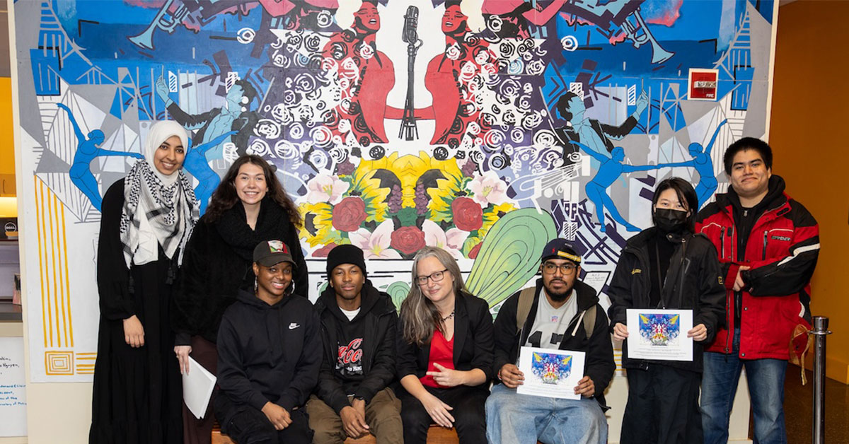 (Left to right) Mawada Ahmed, Juliet Dakin, Latifah Ford, Jose Romain, Adjunct Instructor of Mural Art and Screen Printing Julia Cocuzza, Noah Hinds, Shuqi Li, and Kevin Molina stand in front of the new mural during the dedication ceremony.